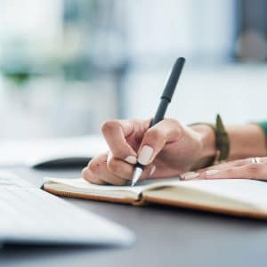 Lady making a list in front of laptop.